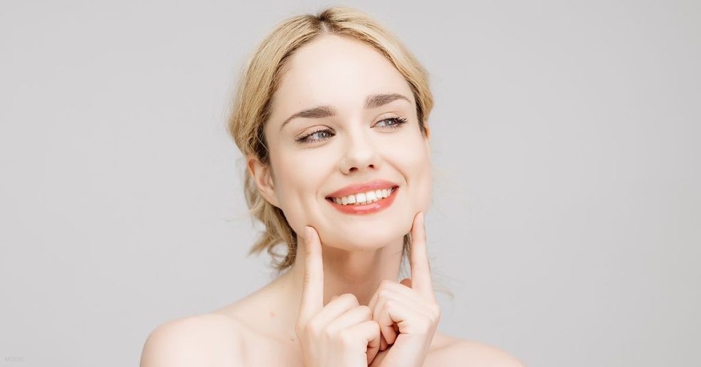 female (model) smiles off into the distance while touching her jawline